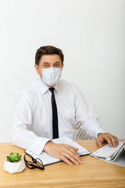 Vírusveszély, szezonális vírusos betegségek. Orvosi maszkban az irodában dolgozó férfi, aki védi az irodai munkásokat a vírusoktól. - Fotó, kép