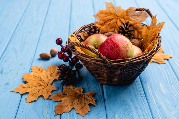 herfst rieten mand met appels en gebladerte op blauwe houten achtergrond - Foto, afbeelding