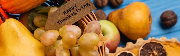 top view of autumnal harvest in wicker basket with happy thanksgiving card near pumpkin pie, panoramic shot - Photo, Image