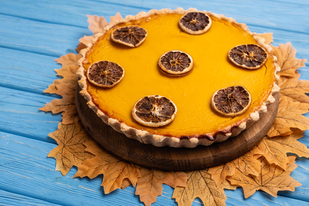 decorated pumpkin pie with golden foliage on blue wooden background - Photo, Image