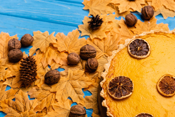top view of pumpkin pie on autumnal foliage with walnuts and cones - Foto, Imagem
