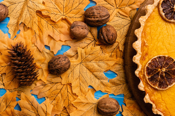 top view of pumpkin pie on autumnal foliage with walnuts and cone - Foto, Imagem