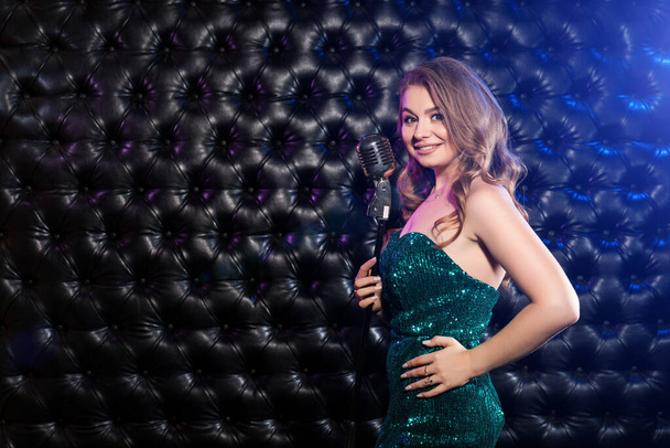 Karaoke konserinde güzel elbiseli, mikrofonlu ve renkli ışıkları olan genç bir kadın. - Fotoğraf, Görsel