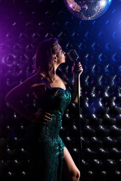 Jovem mulher em vestido bonito com microfone e luzes coloridas no concerto de karaoke - Foto, Imagem