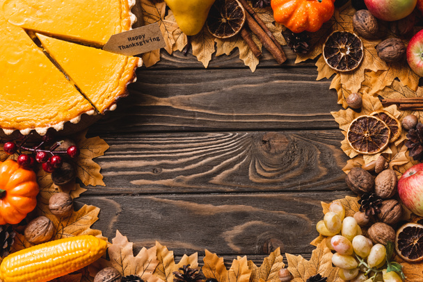 top view of autumnal decoration and pumpkin pie with happy thanksgiving card on brown wooden background - Zdjęcie, obraz