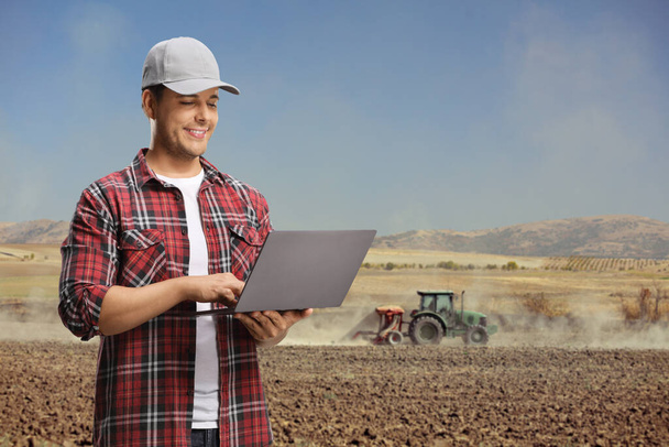 Young agriculture engineer using a laptop computer on a field with a tractor - Foto, afbeelding