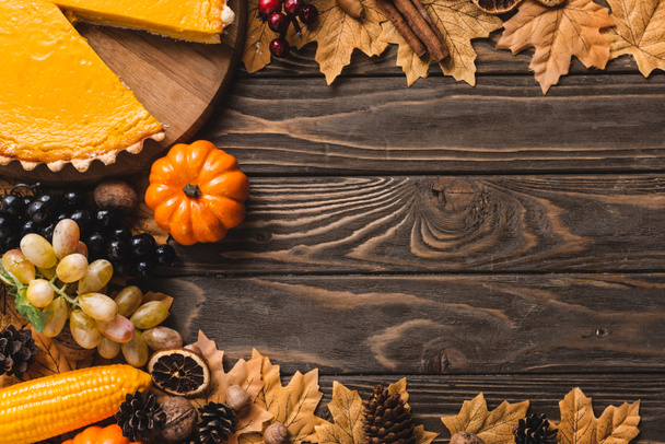 top view of autumnal decoration and pumpkin pie on brown wooden background - Foto, Imagem
