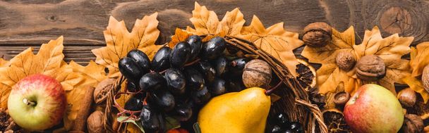 top view of autumnal harvest in basket on foliage on brown wooden background, panoramic shot - Foto, Bild