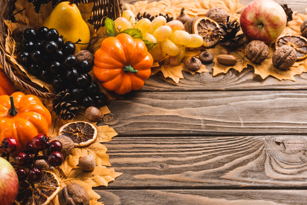 autumnal harvest in basket on foliage on brown wooden background - Foto, afbeelding
