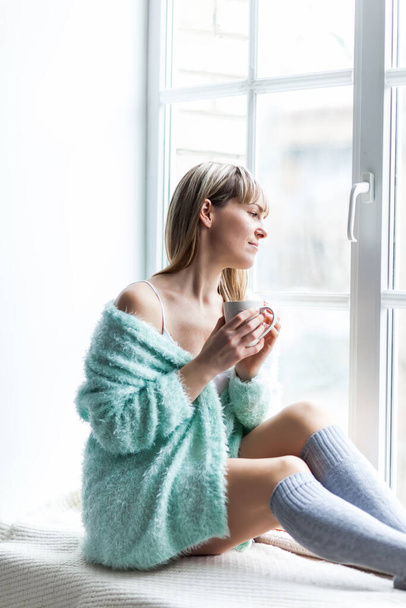 Beautiful woman drinks coffee in the morning. Spring or Autumn sunrise. Coffee cup. Window. Natural wool. - Photo, Image