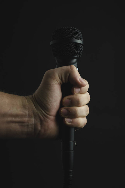 A vertical shot of a person holding a microphone on a black background - Φωτογραφία, εικόνα