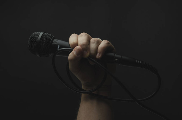 Una persona sosteniendo un micrófono negro sobre un fondo negro - Foto, imagen