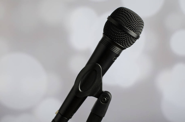 A person holding a black microphone on a grey background with white bokeh lights - Foto, afbeelding