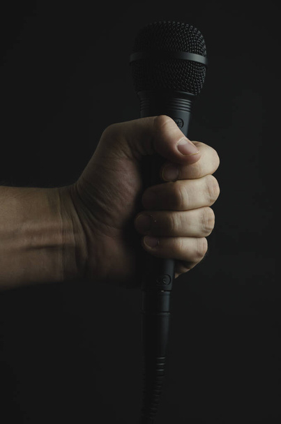 A vertical shot of a person holding a microphone on a black background - Фото, зображення