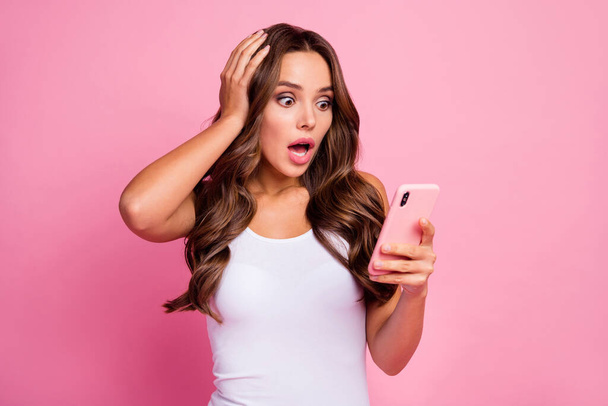 Photo of pretty crazy curly lady open mouth hold telephone read bad negative comments blog arm on head wear white casual singlet isolated pink color background - Foto, immagini