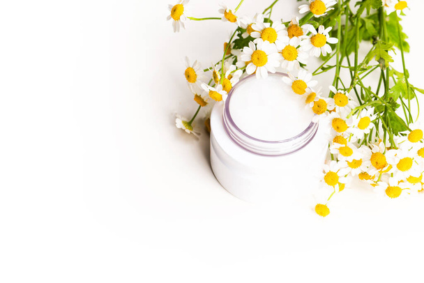 Πλαστικό μπουκαλάκι με άρωμα ή ορό και με λουλούδια χαμομηλιού σε μαρμάρινο ταμπλό. Ενυδατική κρέμα προσώπου και χαμομήλι σε λευκό φόντο - Φωτογραφία, εικόνα