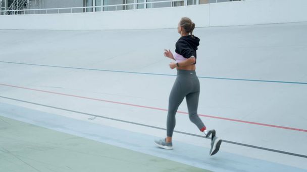 Woman with artificial limb jogging on track. Athlete running on sport stadium - Foto, imagen