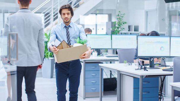 Sad Fired Let Go Office Worker Packs His Belongings into Cardboard Box and Leaves Office. Workforce Reduction, Downsizing, Reorganization, Restructuring, Outsourcing. Mass Unemployment Market Crisis - Photo, Image