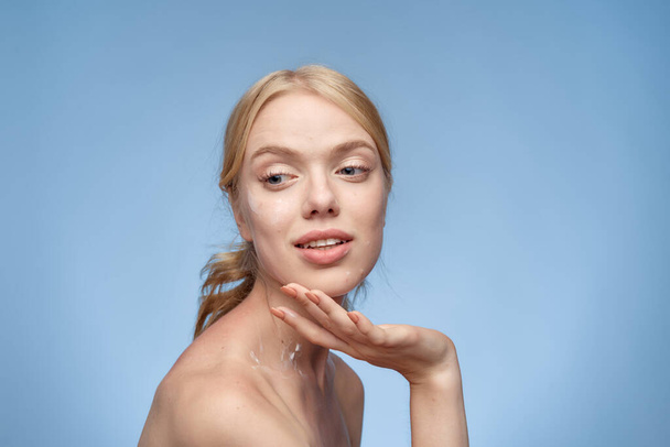 mujer con crema en la cara hombros desnudos cuidado de la piel mano de cerca cerca de la cara fondo azul - Foto, imagen