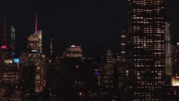 AERIAL: Adembenemend weids uitzicht op het iconische Empire State Building verdwijnen achter residentiële flatgebouwen en kantoorgebouwen in Midtown Manhattan, New York City 's nachts - Video