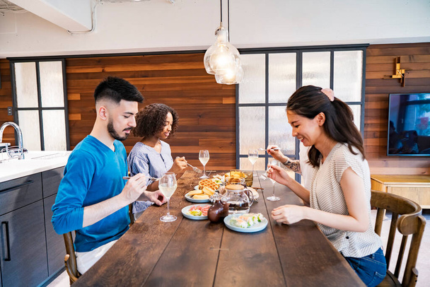 Сцена домашней вечеринки, где мужчины и женщины окружают обеденный стол - Фото, изображение