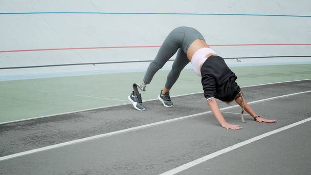 Handicapped woman practicing yoga on stadium. Sportswoman exercising on track - Photo, Image