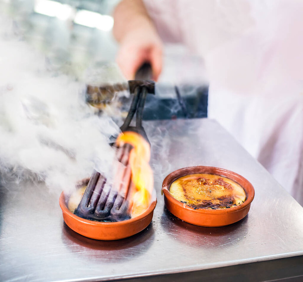 A szakács égető és karamellizáló krém Brulee vagy Crema Catalana rusztikus tálban. Hagyományos desszert Franciaországban és Katalóniában, Spanyolországban. - Fotó, kép