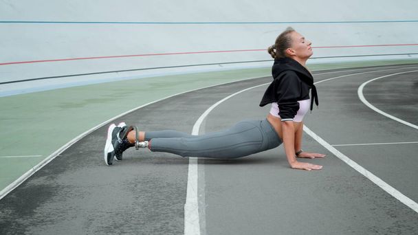 Behinderte Frau praktiziert Yoga im Sportstadion. Mädchen beim Sport im Freien - Foto, Bild