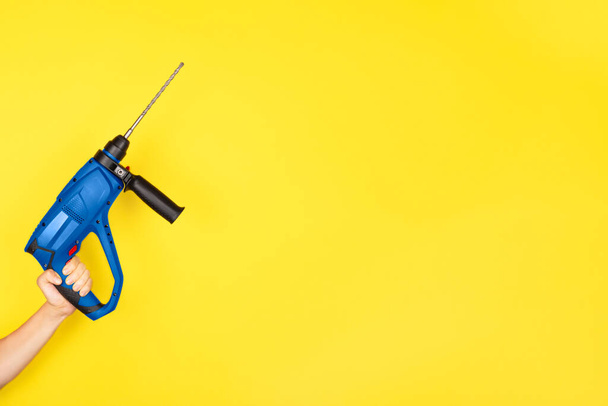 Blue Puncher in the hands of a builder. Female hand hold new Puncher or drill isolated on yellow background. Banner with copy space. - Photo, Image