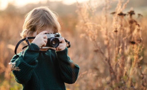 Маленька дівчинка в осінній природі, фотографується з фотоапаратом
. - Фото, зображення