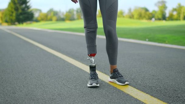 Niepełnosprawny sportowiec rozgrzewający nogi przed treningiem w parku. Szkolenie kobiet na świeżym powietrzu - Zdjęcie, obraz