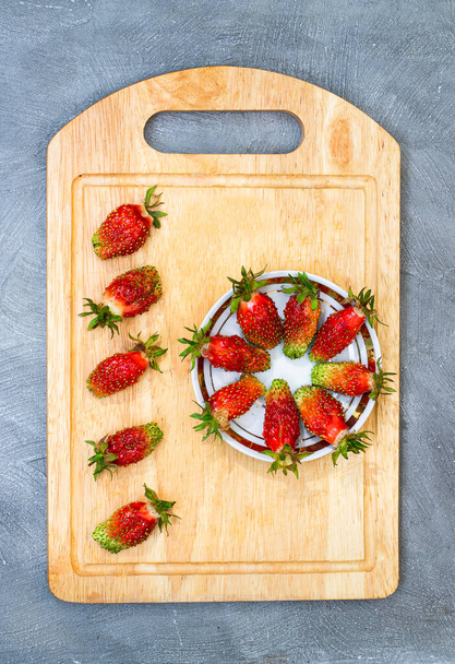 Strawberry berries on a white plate on a cutting Board on a gray background. The view from the top. - Fotó, kép
