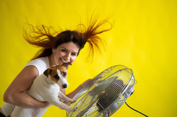 Redhead caucasian woman and a dog are cooling off by an electric fan.  - Fotó, kép