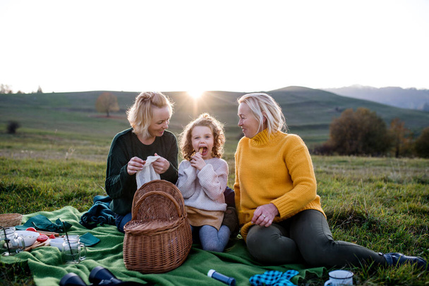 Small girl with mother and grandmother having picnic in nature at sunset. - Valokuva, kuva