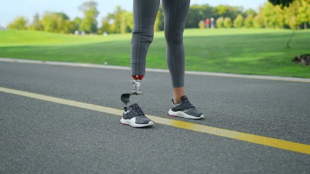 Corredor con extremidad artificial de pie en el parque. Mujer en posición de salida en la carretera - Foto, imagen