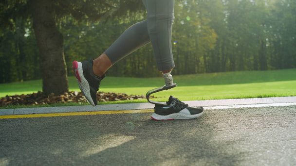 Spor ayakkabılı engelli bir kadın yolda koşuyor. Kız ayakları dışarıda çalışıyor. - Fotoğraf, Görsel
