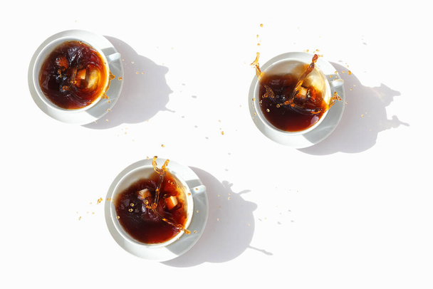 Black coffee in white cups, top view. Sugar lumps are thrown into the cup, spectacular splashes are spilling out of the cup. White background. - Photo, image