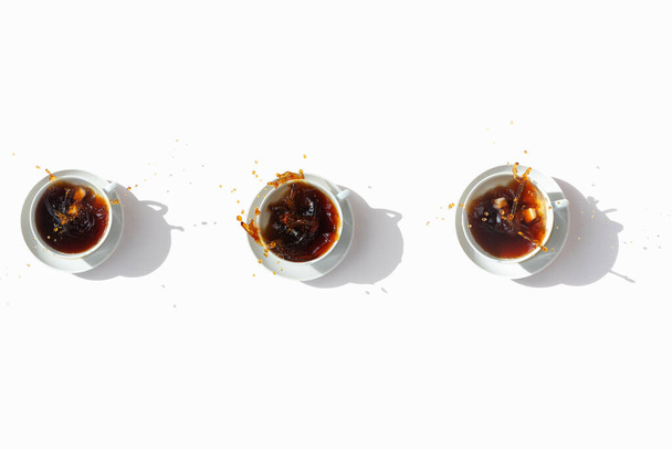 Black coffee in white cups, top view. Sugar lumps are thrown into the cup, spectacular splashes are spilling out of the cup. White background. International coffee day. - Fotografie, Obrázek