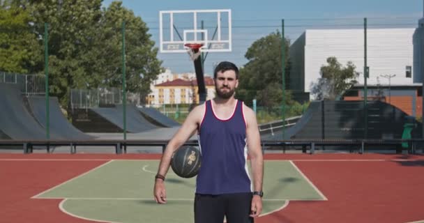Миллениальный баскетболист держит мяч, позирует на открытой площадке - Кадры, видео