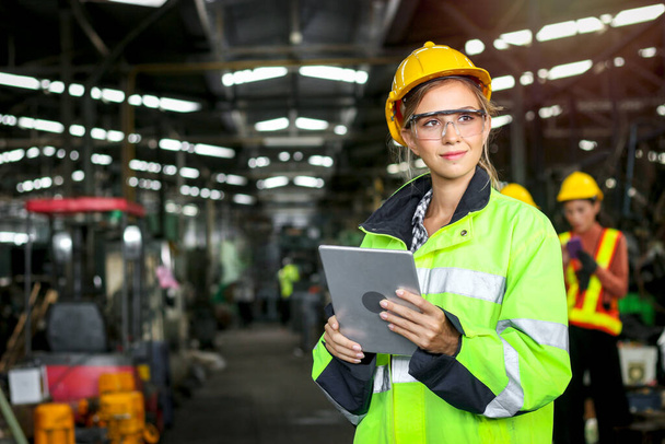 Młoda piękna kobieta inżynier przemysłowy pracownik nosić bezpiecznie kask i odzież ochronna trzymając cyfrowy tablet do obsługi maszyn w fabryce zakładu produkcyjnego, koncepcja pracy przemysłu - Zdjęcie, obraz