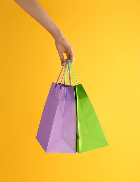 Woman with paper shopping bags on yellow background, closeup - Foto, Bild