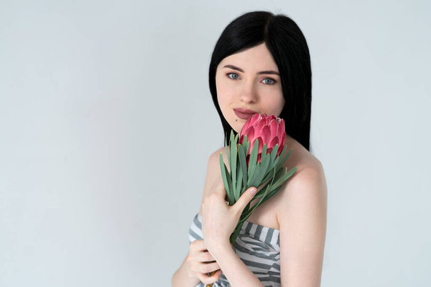 Retrato de una hermosa chica de cabello oscuro y maquillaje natural con una flor de protea en sus manos. - Foto, Imagen