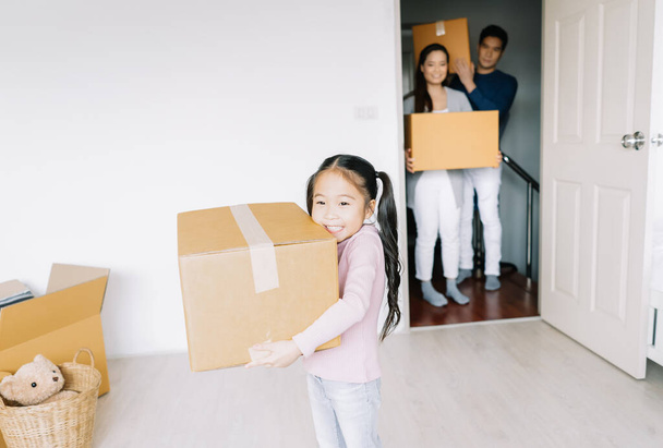 Ritratto di una felice figlia asiatica che porta scatole in una nuova casa il giorno del trasloco. Happy Family passa a un nuovo concetto di casa, aiutando i genitori con effetti personali, mutuo e trasferimento. - Foto, immagini