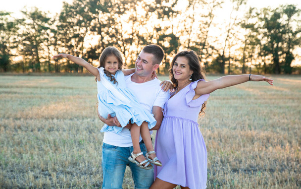 happy young family on the field, pregnant wife and a little girl hugs with father - Φωτογραφία, εικόνα