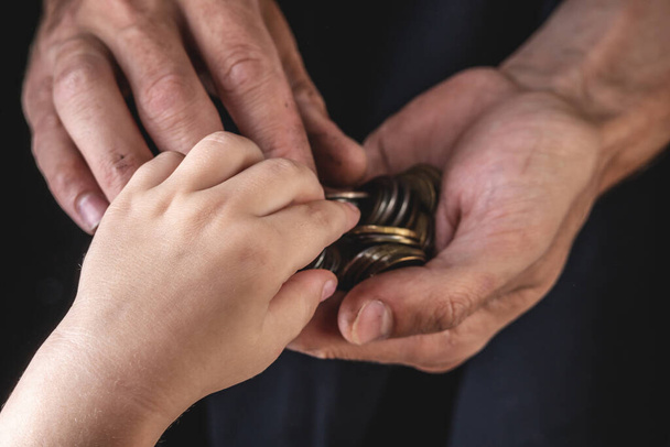 As mãos de homens mantêm moedas de rublo close-up em um fundo escuro. A mão de uma criança estende-se à procura de ajuda. O conceito de pobreza e miséria - Foto, Imagem