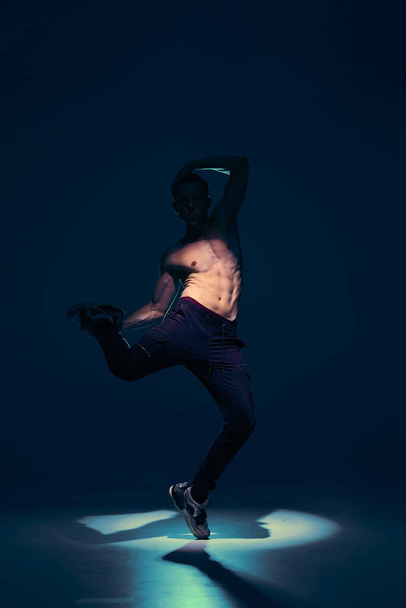 Young man dancer without shirt dancing in studio in the spotlight. Dance school poster - Photo, image