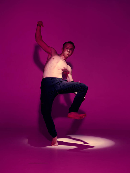 Cool young guy dancer with naked torso dancing in studio in pink light. Dance school poster - Fotó, kép