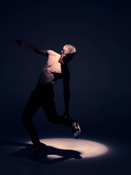 Cool young guy dancer with naked torso dancing in studio in the spotlight. Dance school poster - Fotó, kép