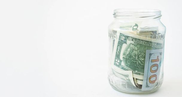 Piggy bank from a glass jar with new dollars for life on a white background. Copy space. Economy concept. - Photo, Image