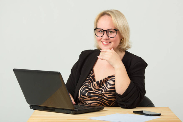 beautiful young woman on a white background in glasses at the table with a laptop - Valokuva, kuva